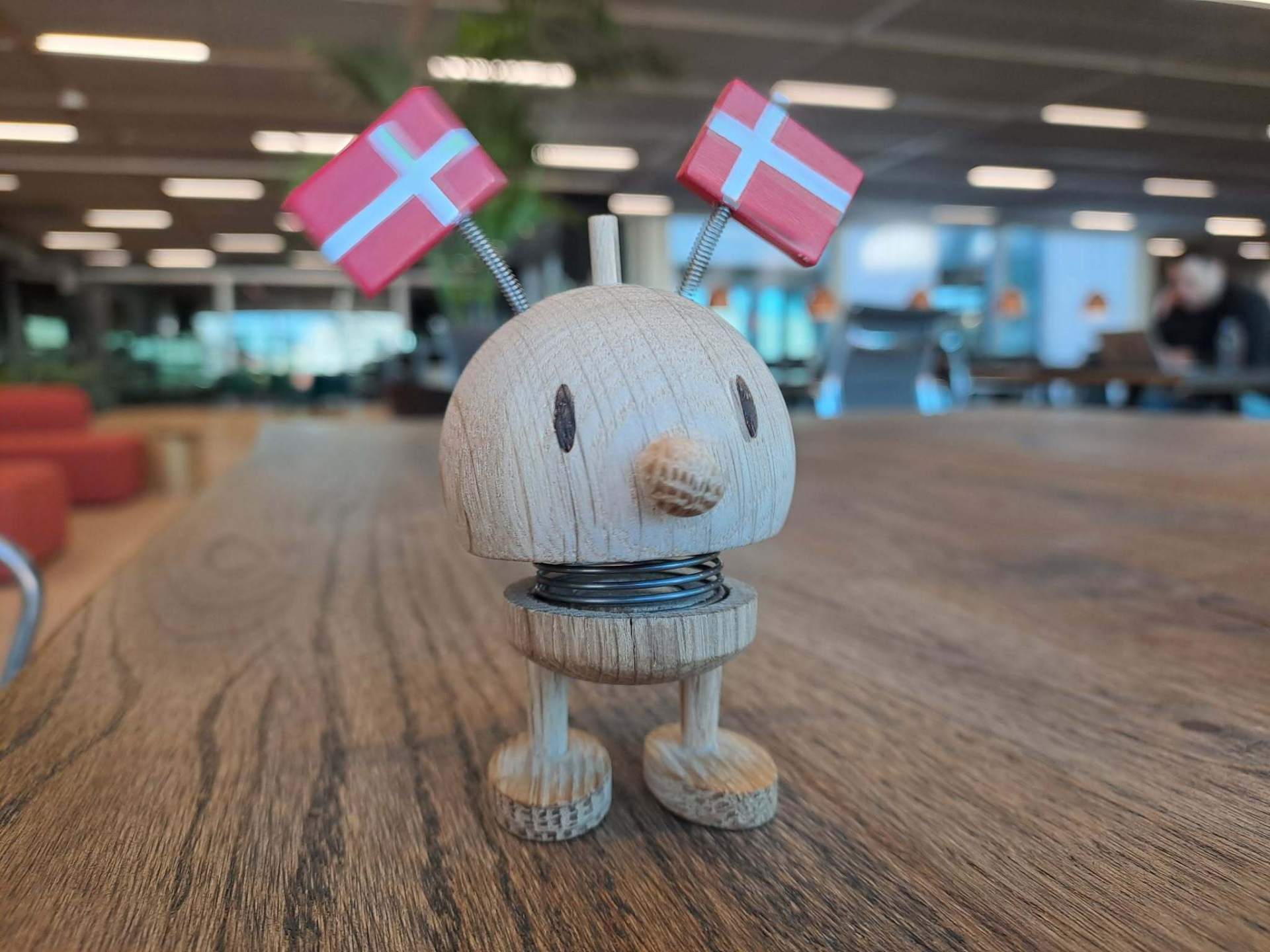 Hans, a small red smiley Hoptimist figurine on a wooden table